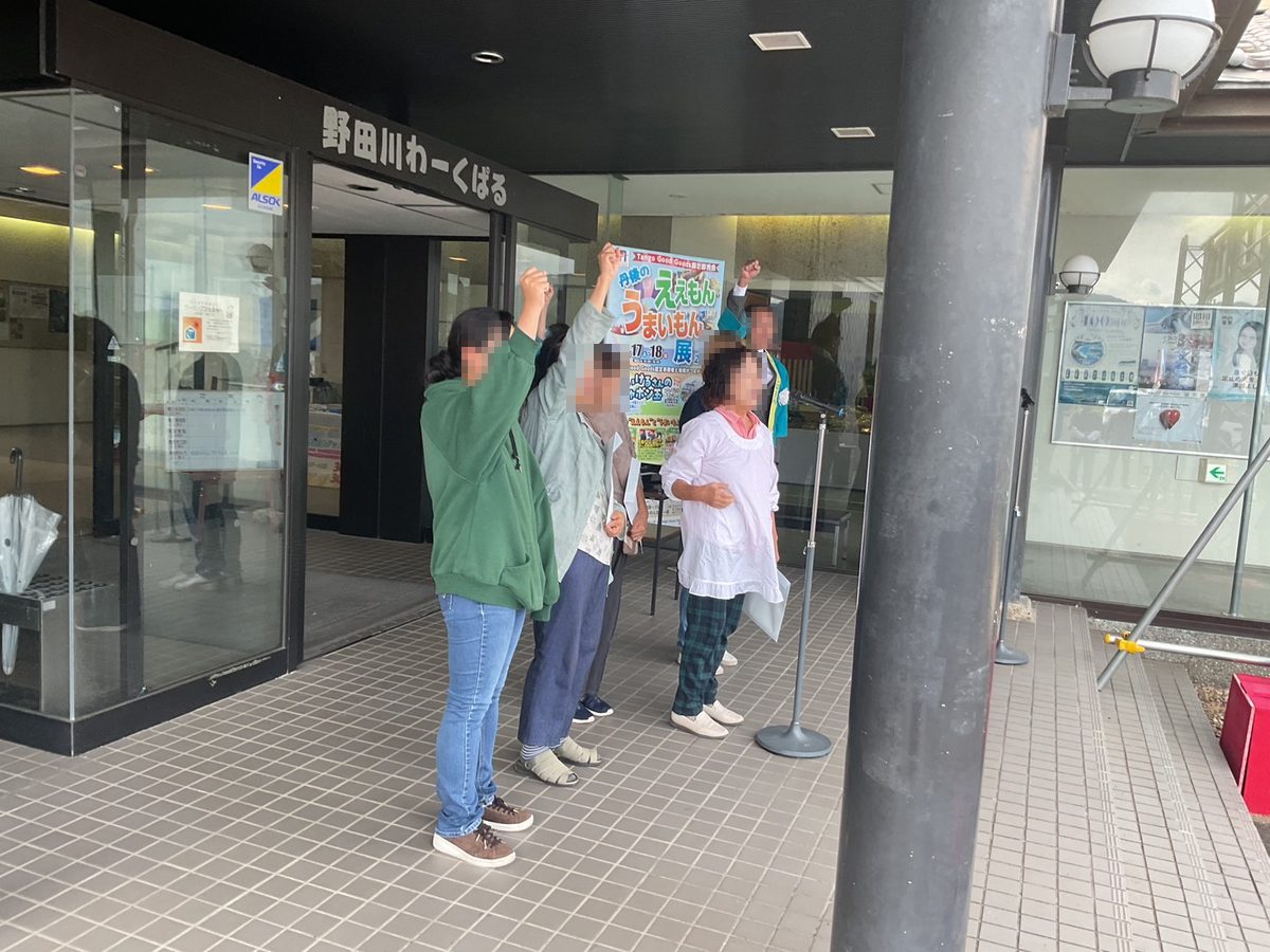 会場の入口で、ポスターを囲んでこぶしを上げる様子